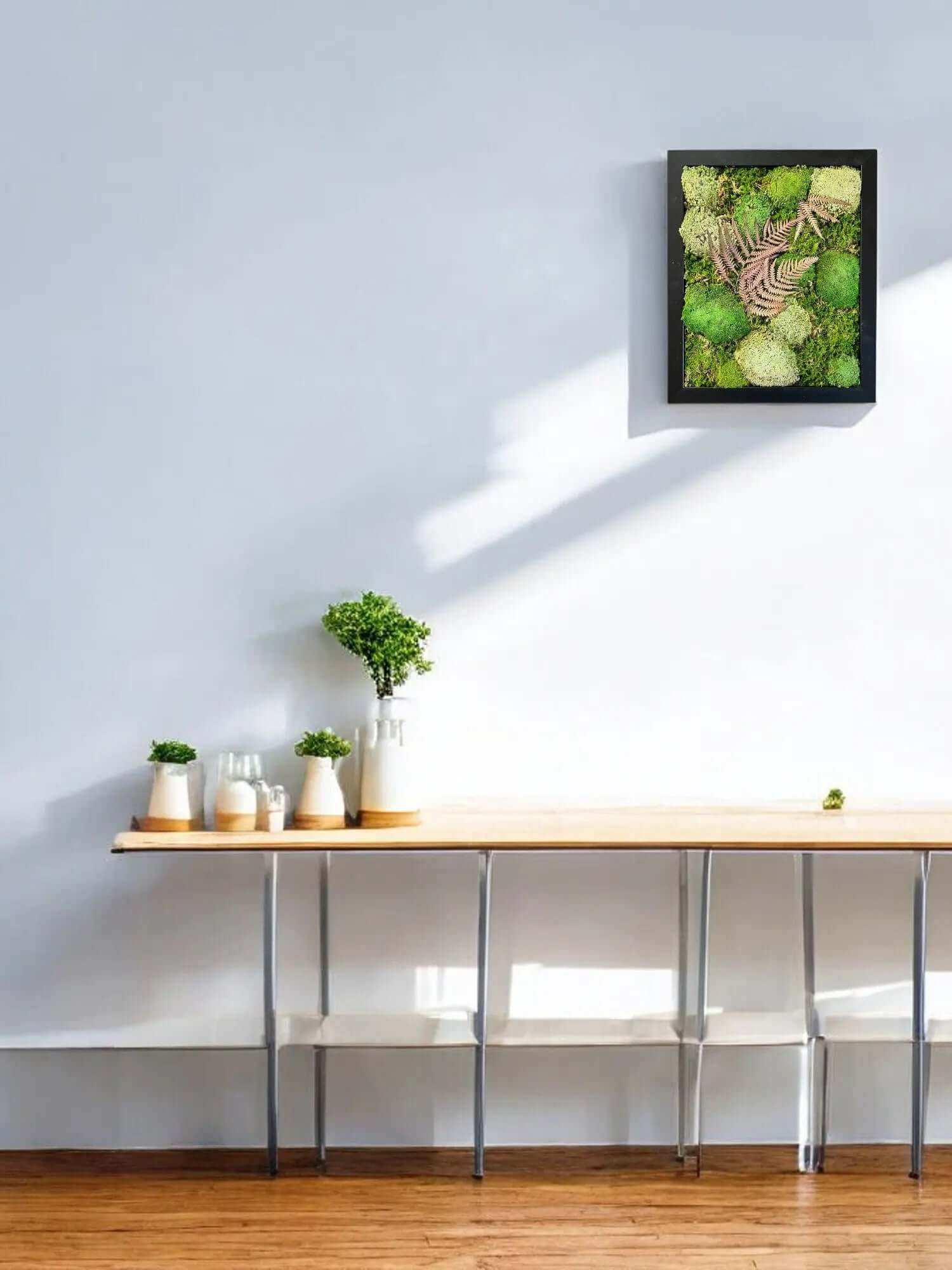 Preserved moss wall art with leaves hanging above a console table in a modern living room.