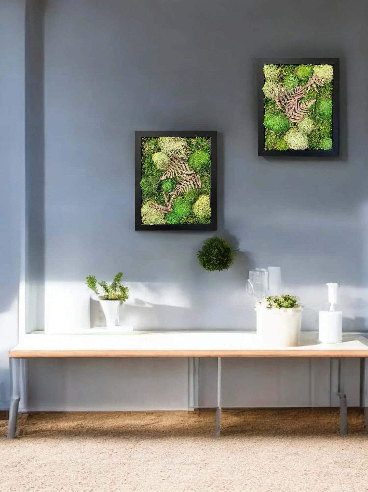 Preserved moss wall art with leaves hanging above a side table with decorative plants and home decor objects on top