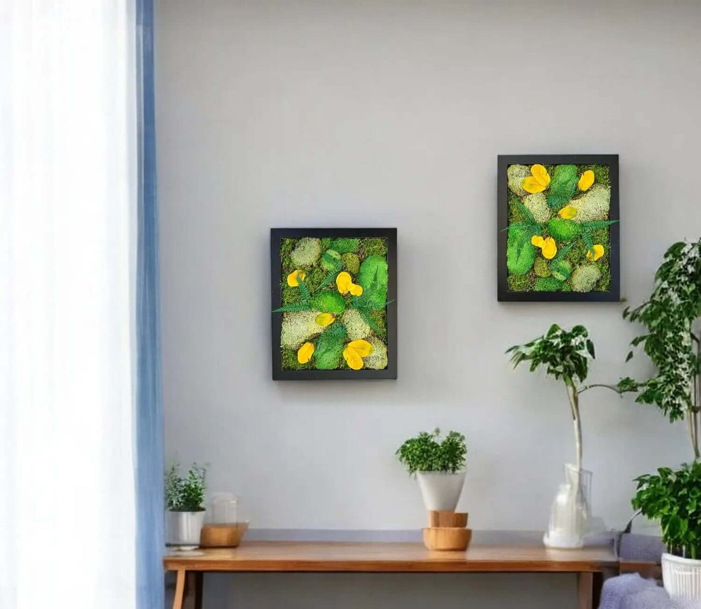 Preserved moss wall art hanging above a side table with decorative plants and home decor objects on top