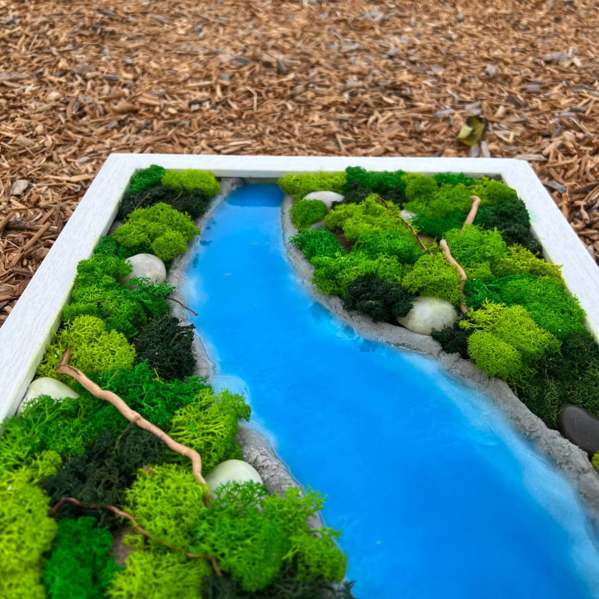 nique wall decor featuring a sky-blue epoxy river design, nestled amongst preserved moss and natural rocks on a bed of wood chips. A captivating piece that brings the outdoors in